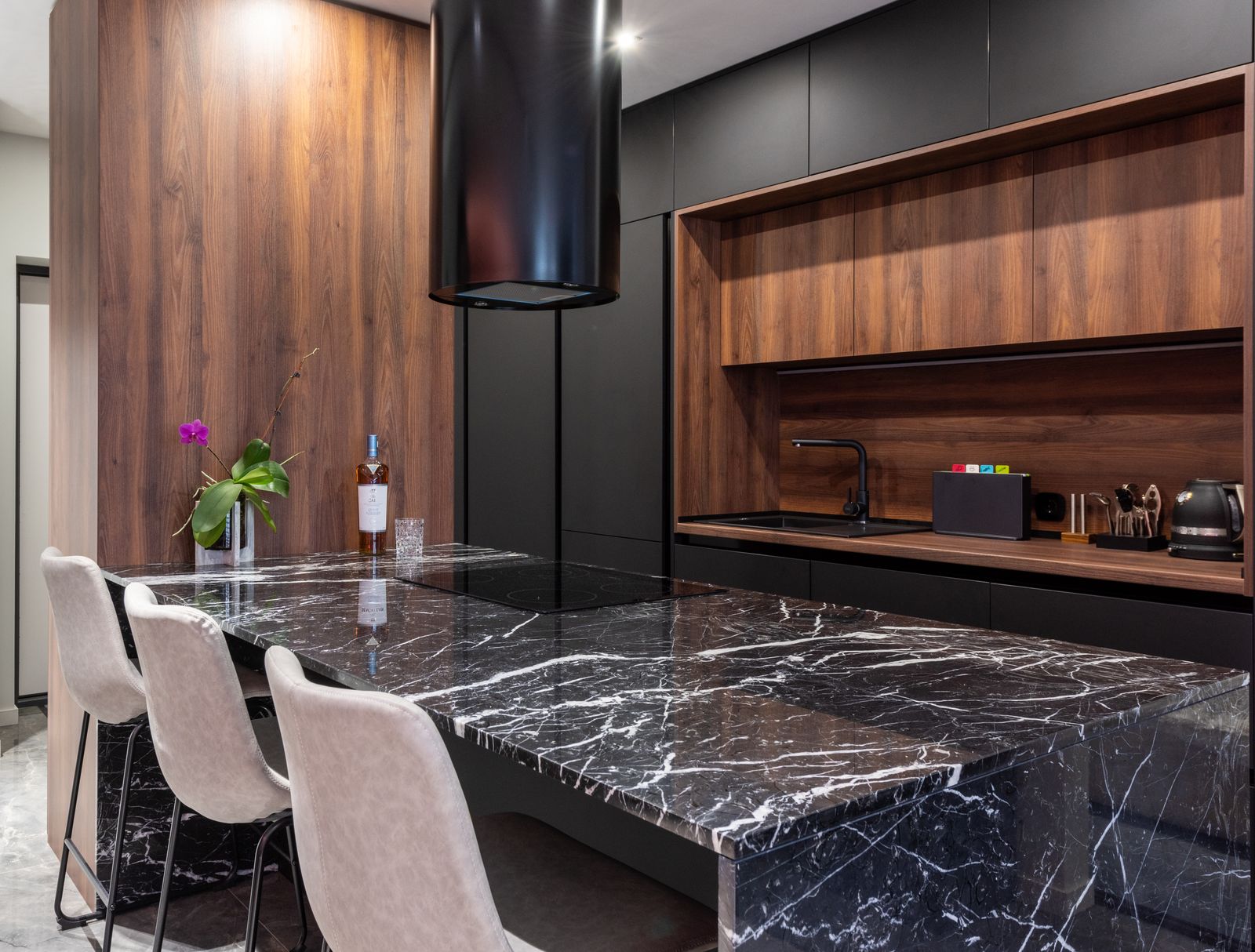 Modern kitchen with bottle on marble table under hood against electric appliances in light house